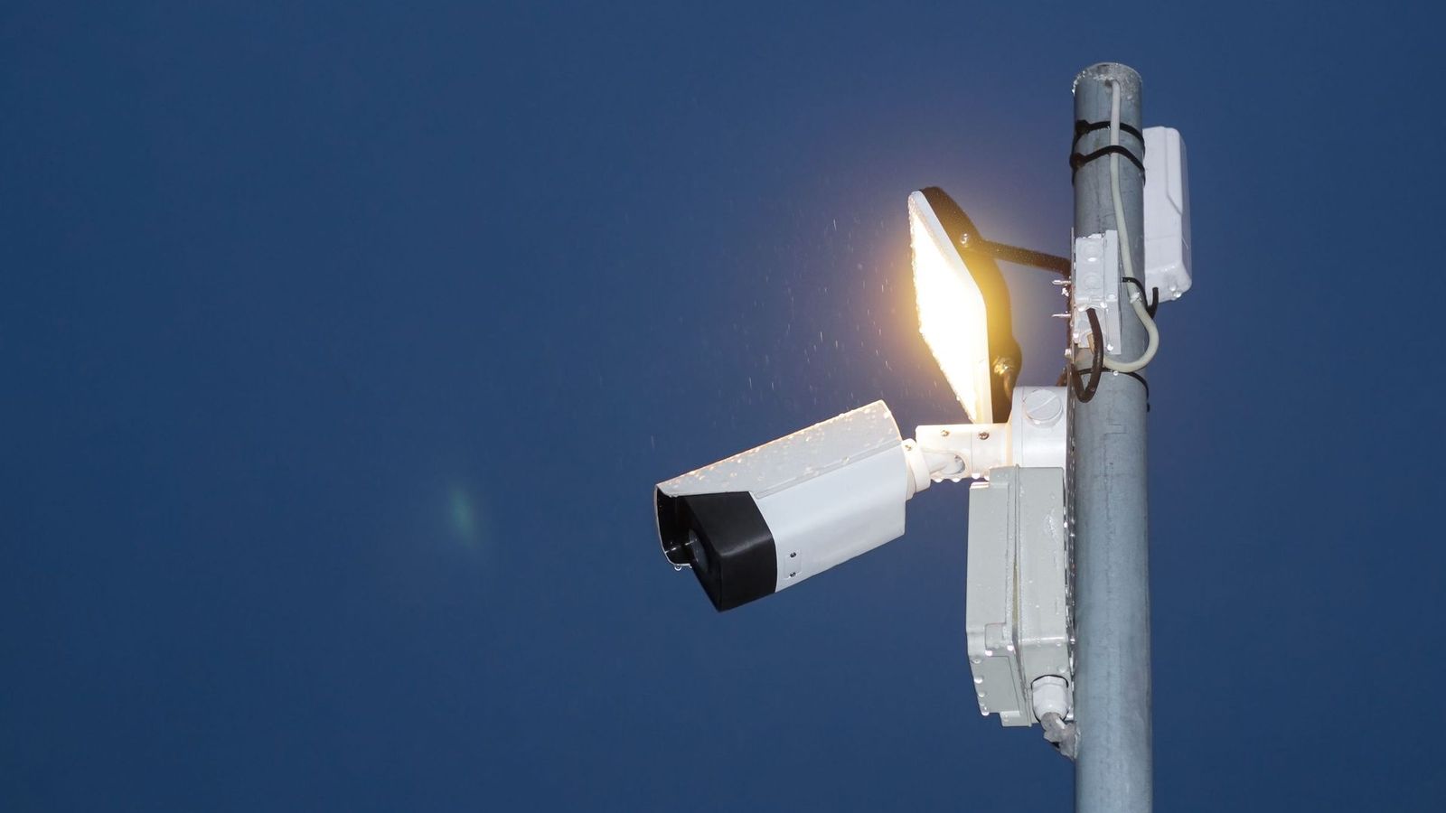 Beveiligingscamera en schijnwerper aan een mast tegen een nachtelijke hemel